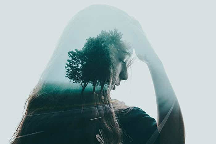 Beautiful and atmospheric double exposure of a girl with her hand to your head, layered with a photo of trees lining a roadway